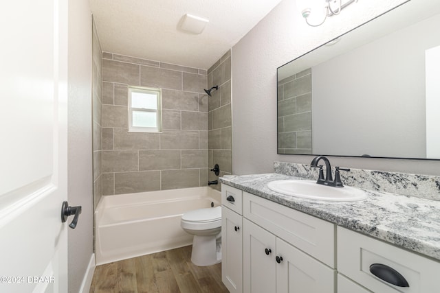 full bathroom featuring toilet, hardwood / wood-style floors, a textured ceiling, tiled shower / bath combo, and vanity