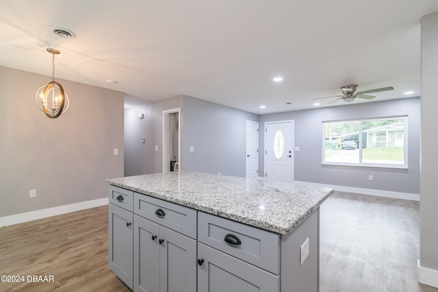 kitchen with light hardwood / wood-style floors, light stone countertops, ceiling fan with notable chandelier, decorative light fixtures, and a kitchen island