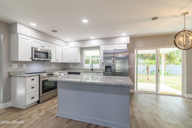 kitchen featuring stainless steel appliances, light hardwood / wood-style floors, light stone countertops, white cabinetry, and decorative light fixtures