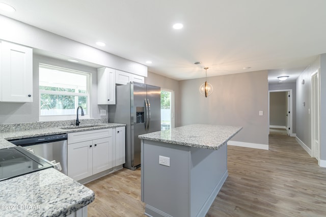 kitchen with light hardwood / wood-style floors, white cabinets, sink, a kitchen island, and pendant lighting