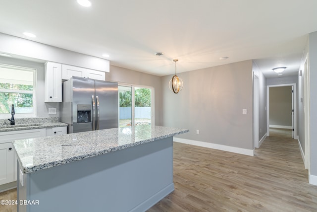 kitchen featuring light wood-type flooring, hanging light fixtures, stainless steel refrigerator with ice dispenser, sink, and white cabinets