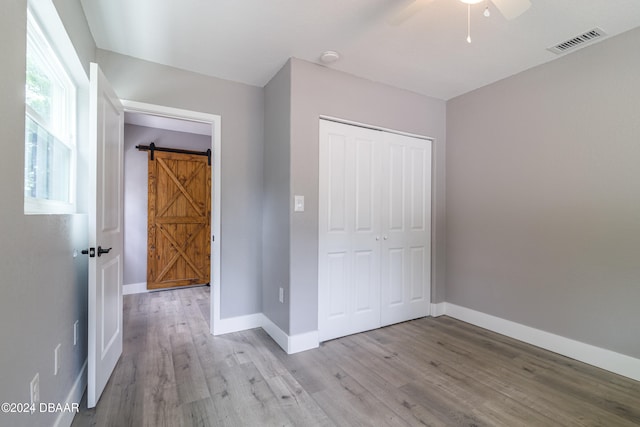 unfurnished bedroom with a barn door, ceiling fan, a closet, and light hardwood / wood-style flooring