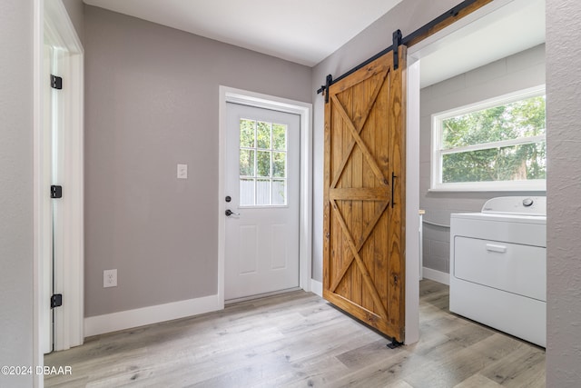 entryway with a barn door, washer / dryer, a healthy amount of sunlight, and light hardwood / wood-style flooring