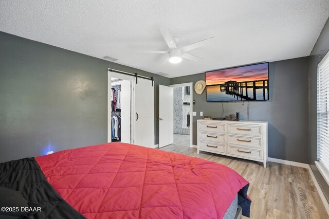 2950 Ragis Rd, Edgewater, FL 32132 - bedroom with a barn door, light wood-style floors, a textured ceiling, a spacious closet, and ensuite bath