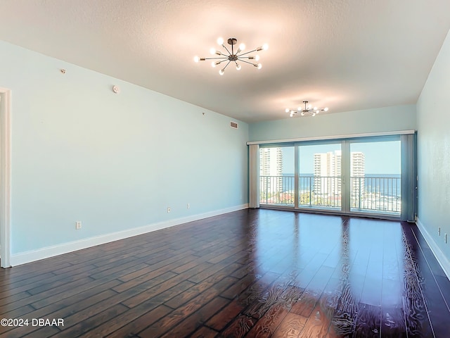 empty room with a textured ceiling, dark hardwood / wood-style flooring, and a notable chandelier