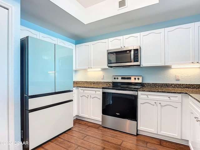 kitchen featuring dark hardwood / wood-style flooring, white cabinetry, appliances with stainless steel finishes, and dark stone counters