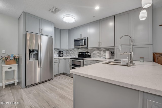 kitchen featuring appliances with stainless steel finishes, light hardwood / wood-style flooring, gray cabinetry, pendant lighting, and decorative backsplash