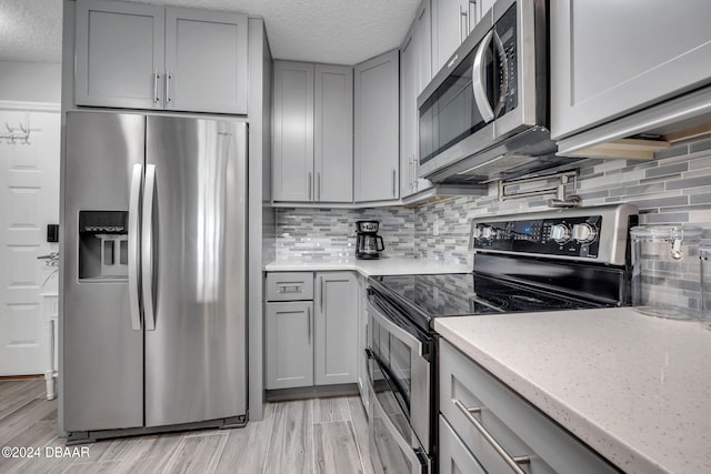 kitchen featuring tasteful backsplash, light stone countertops, appliances with stainless steel finishes, and light hardwood / wood-style floors