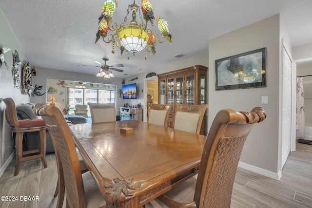 dining area with ceiling fan with notable chandelier, a textured ceiling, and light hardwood / wood-style flooring