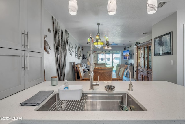 kitchen with pendant lighting, sink, light stone countertops, and a textured ceiling