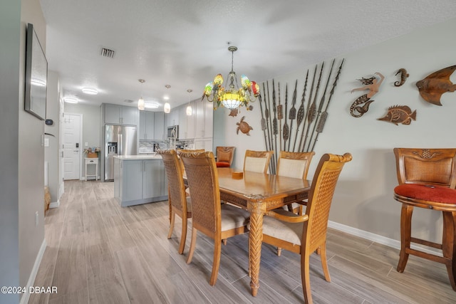 dining space with a textured ceiling, light hardwood / wood-style flooring, and a notable chandelier