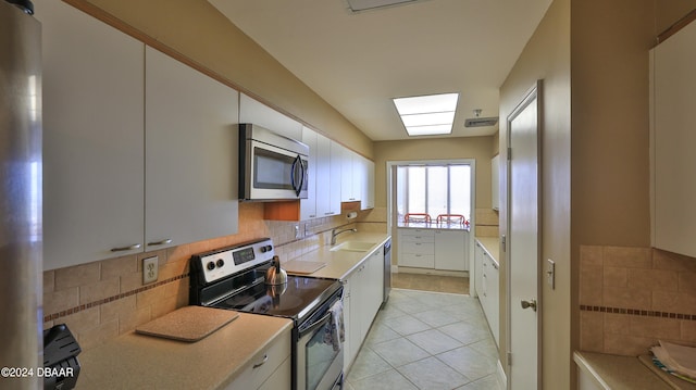 kitchen with sink, light tile patterned flooring, backsplash, white cabinetry, and appliances with stainless steel finishes