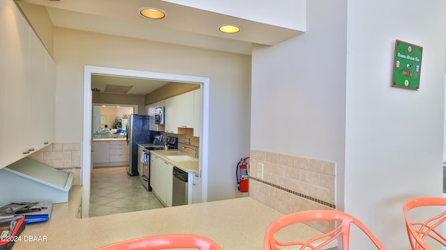 kitchen with stainless steel appliances, light tile patterned flooring, sink, white cabinets, and decorative backsplash