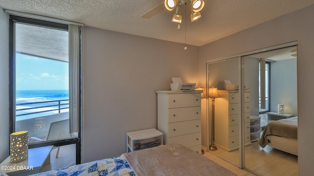 bedroom featuring light hardwood / wood-style floors, a water view, a textured ceiling, ceiling fan, and a closet