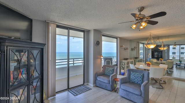 living room featuring light wood-type flooring, ceiling fan, a textured ceiling, and a water view