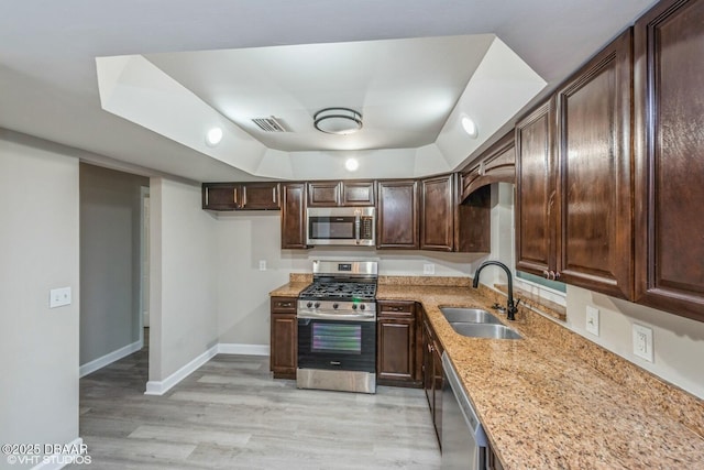 kitchen featuring light stone countertops, dark brown cabinetry, stainless steel appliances, sink, and light hardwood / wood-style flooring