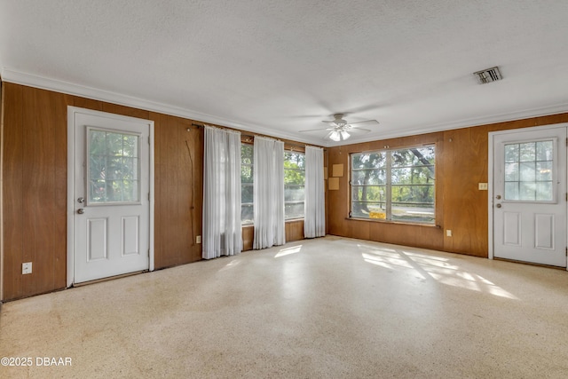 interior space with crown molding, ceiling fan, a textured ceiling, and wood walls