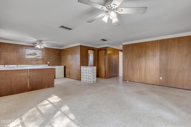 unfurnished living room with crown molding, ceiling fan, and wooden walls