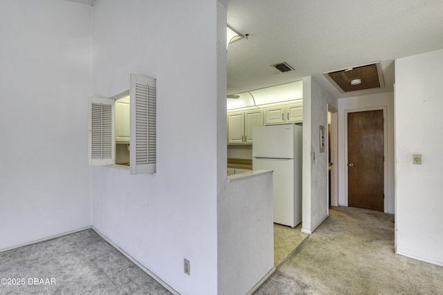 hallway with light carpet, visible vents, and a textured ceiling