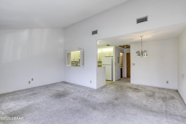 empty room featuring visible vents, light carpet, a chandelier, and vaulted ceiling