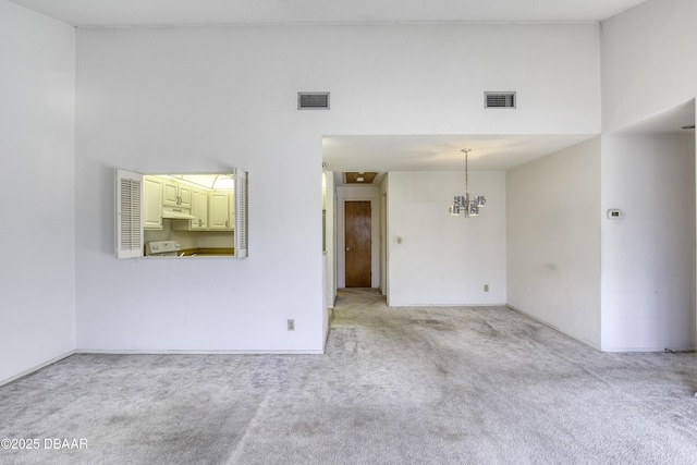 unfurnished room featuring an inviting chandelier, light colored carpet, visible vents, and a towering ceiling