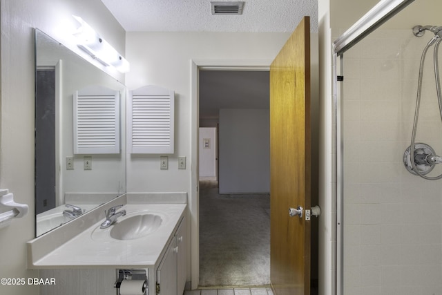 bathroom with vanity, tiled shower, visible vents, and a textured ceiling