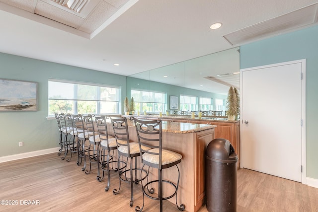 kitchen with light stone counters, a kitchen bar, light wood-style flooring, and baseboards