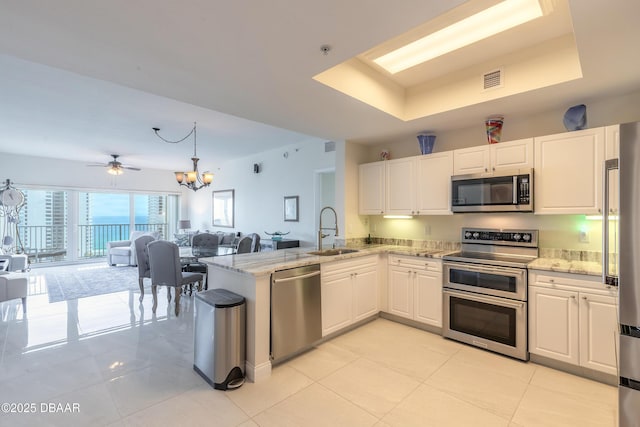 kitchen featuring a tray ceiling, a sink, white cabinets, appliances with stainless steel finishes, and open floor plan