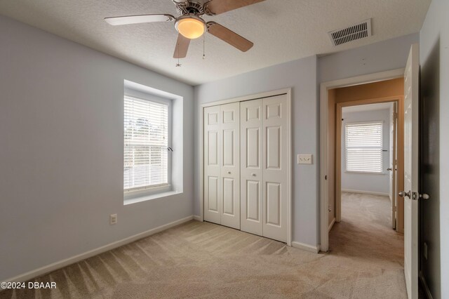 unfurnished bedroom featuring a closet, a textured ceiling, light carpet, and ceiling fan