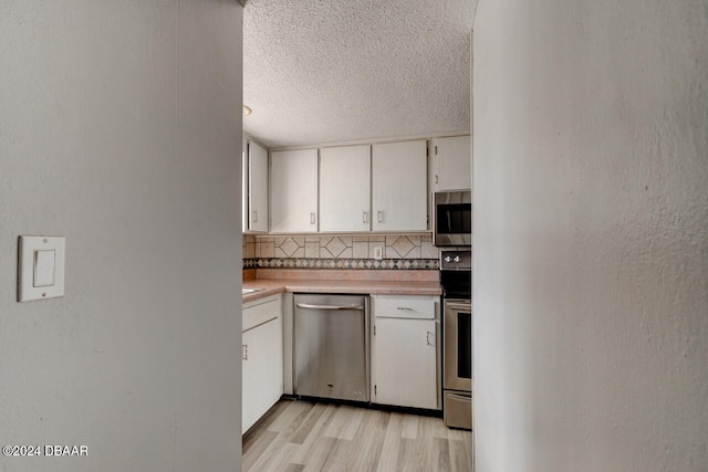 kitchen featuring white cabinetry, stainless steel appliances, tasteful backsplash, light hardwood / wood-style flooring, and a textured ceiling