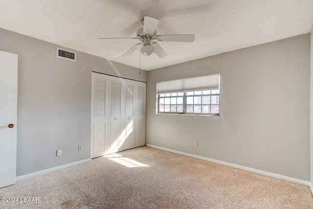 unfurnished bedroom featuring ceiling fan, a closet, light colored carpet, and a textured ceiling