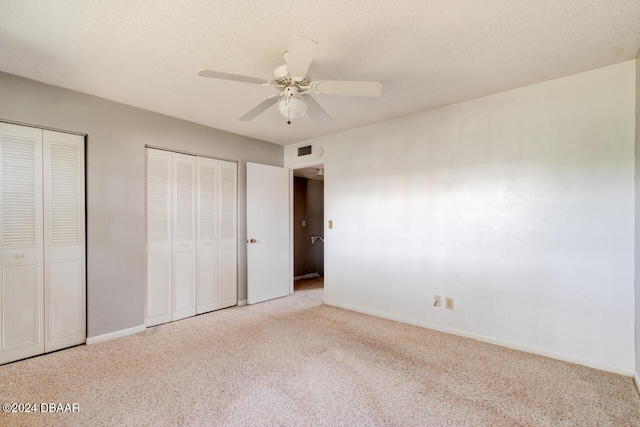 unfurnished bedroom featuring a textured ceiling, ceiling fan, light carpet, and two closets