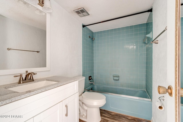 full bathroom with vanity, hardwood / wood-style flooring, tiled shower / bath combo, toilet, and a textured ceiling