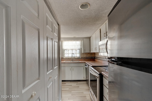 kitchen featuring decorative backsplash, stainless steel appliances, sink, light hardwood / wood-style flooring, and white cabinets