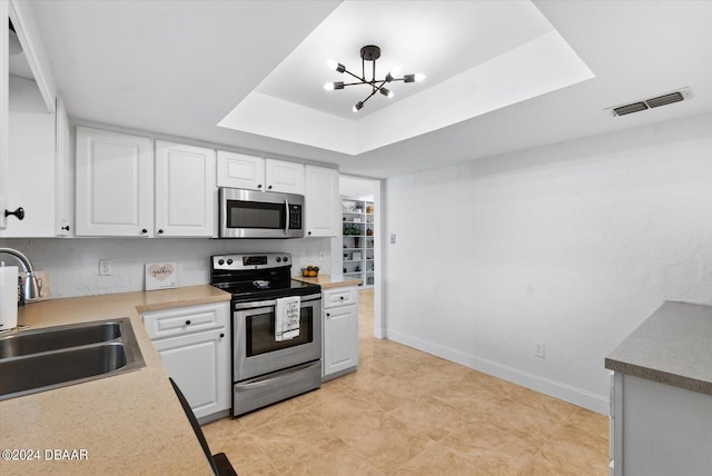 kitchen featuring white cabinets, a notable chandelier, sink, a raised ceiling, and appliances with stainless steel finishes