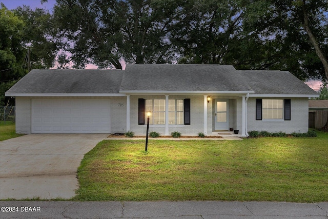 ranch-style home featuring a garage, a porch, and a yard