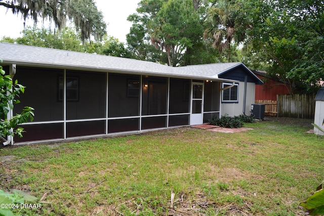 rear view of house with central air condition unit, a sunroom, and a yard