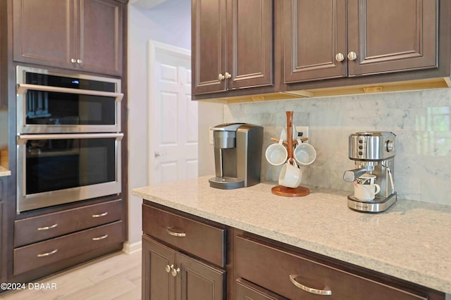 kitchen featuring dark brown cabinetry, light hardwood / wood-style floors, tasteful backsplash, and stainless steel double oven