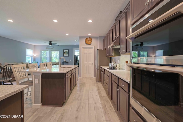 kitchen featuring light hardwood / wood-style floors, sink, an island with sink, a kitchen breakfast bar, and dark brown cabinets