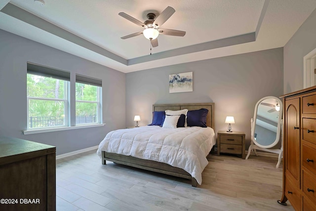 bedroom featuring light hardwood / wood-style floors, ceiling fan, and a raised ceiling