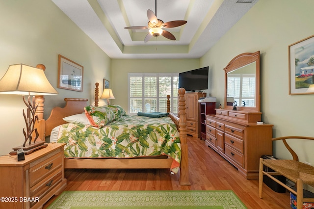 bedroom featuring a raised ceiling, ceiling fan, and light hardwood / wood-style floors