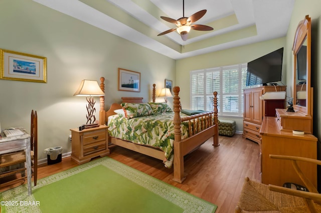 bedroom with hardwood / wood-style flooring, ceiling fan, and a raised ceiling