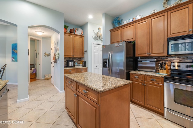 kitchen with tasteful backsplash, a kitchen island, light stone countertops, and appliances with stainless steel finishes