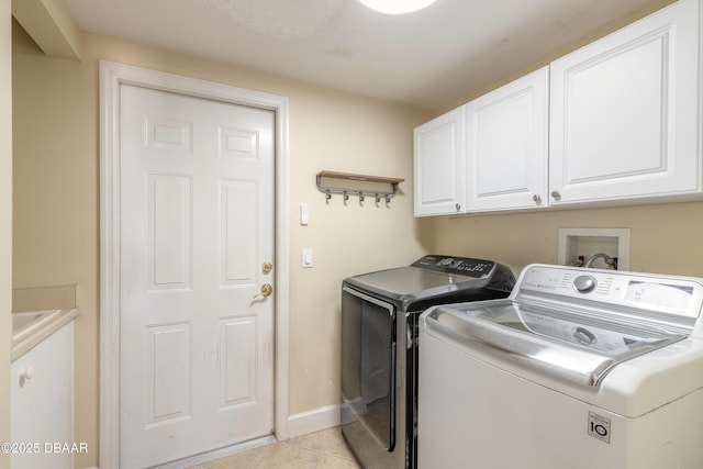 clothes washing area with separate washer and dryer, light tile patterned floors, and cabinets