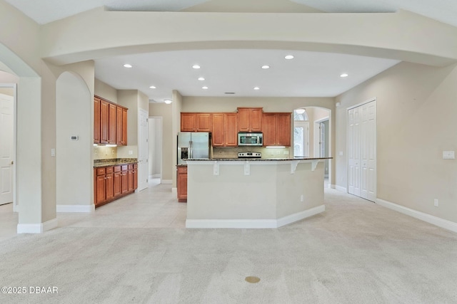 kitchen with a breakfast bar, stainless steel appliances, light carpet, and a center island with sink