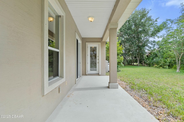 view of exterior entry featuring a patio and a lawn