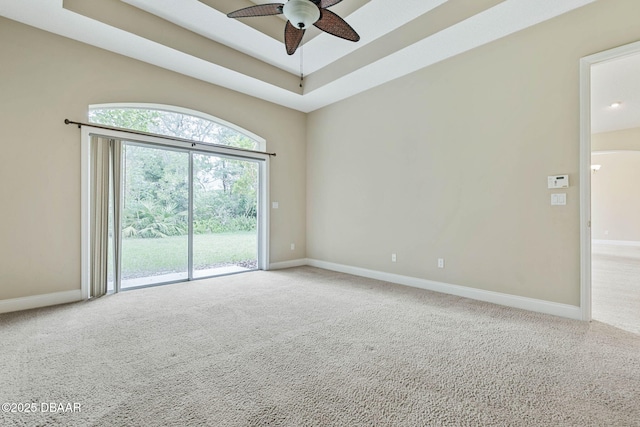 empty room featuring a raised ceiling, ceiling fan, and carpet flooring