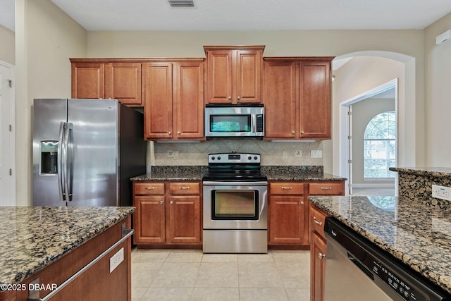 kitchen with appliances with stainless steel finishes, dark stone counters, decorative backsplash, and light tile patterned floors