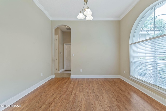 spare room with an inviting chandelier, ornamental molding, and light hardwood / wood-style flooring