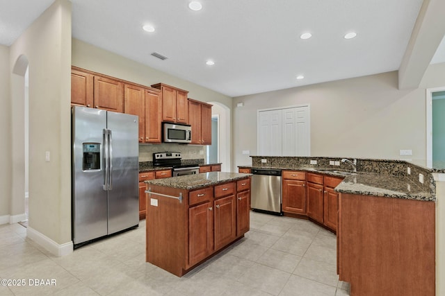 kitchen with kitchen peninsula, stainless steel appliances, a kitchen island, dark stone counters, and sink